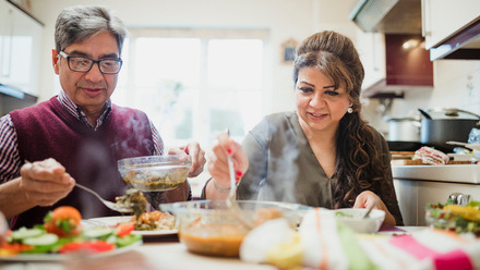 Mature couple are enjoying a homemade curry with salad at home.